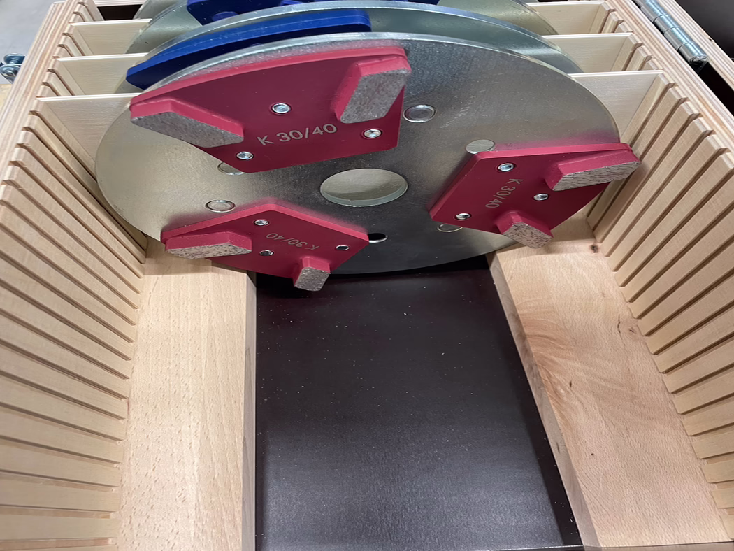 Derendinger_application_10839_milling Nahaufnahme eines runden Metallfräskopfs für die Holzbearbeitung mit drei roten, austauschbaren Hartmetallsegmenten mit der Kennzeichnung K 30/40, stehend in einer Holzkiste mit geschlitzten Trennwänden; das Werkzeug liegt über einer dunklen Arbeitsfläche.