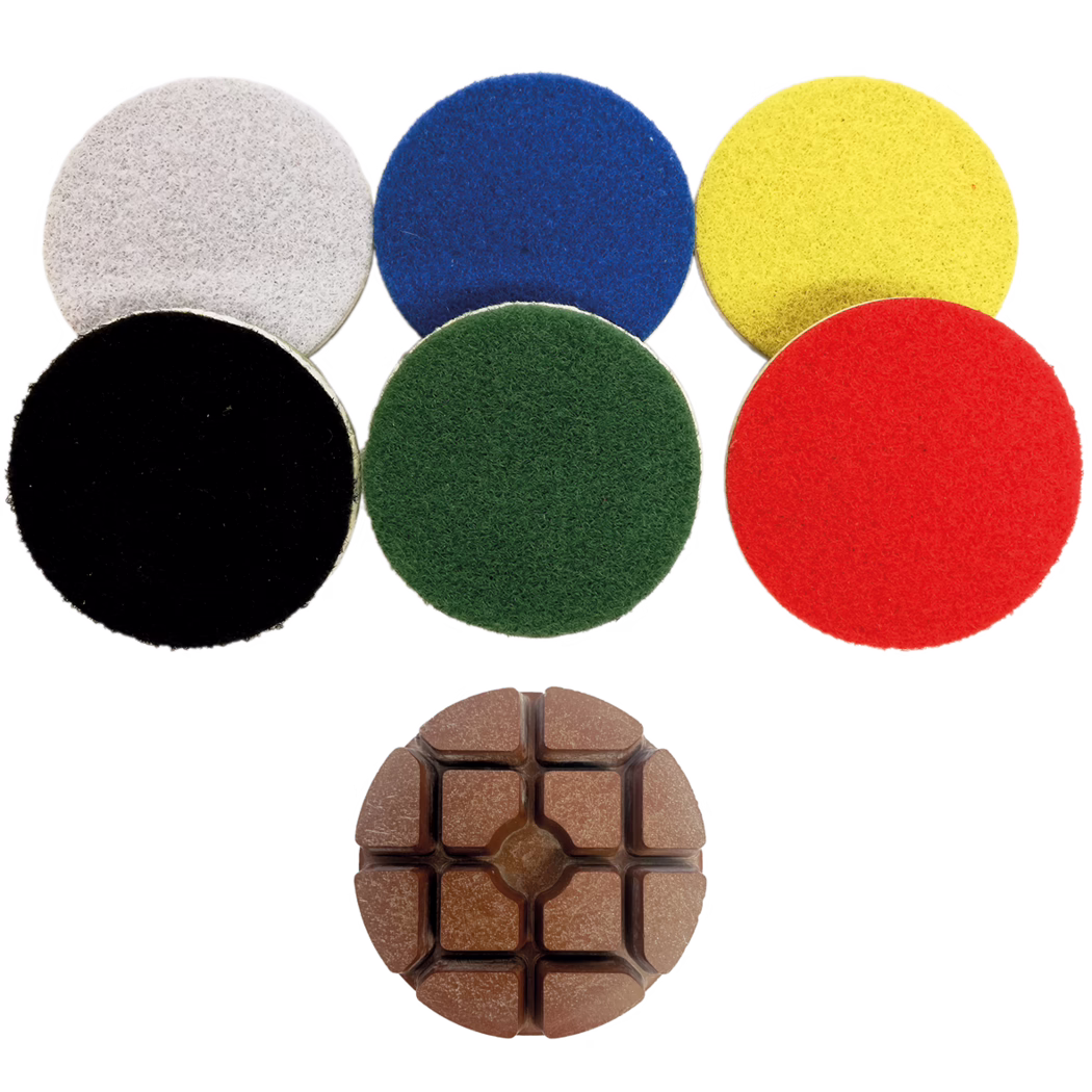 Derendinger_Dummy_10734_Polierpad_Area_oben_2019.12 Eine Sammlung von sechs runden Scheuerpads in verschiedenen Farben: grau, blau, gelb, rot, grün und schwarz, angeordnet in zwei Reihen mit einem braunen multifunktionalen Reinigungswerkzeug darunter.