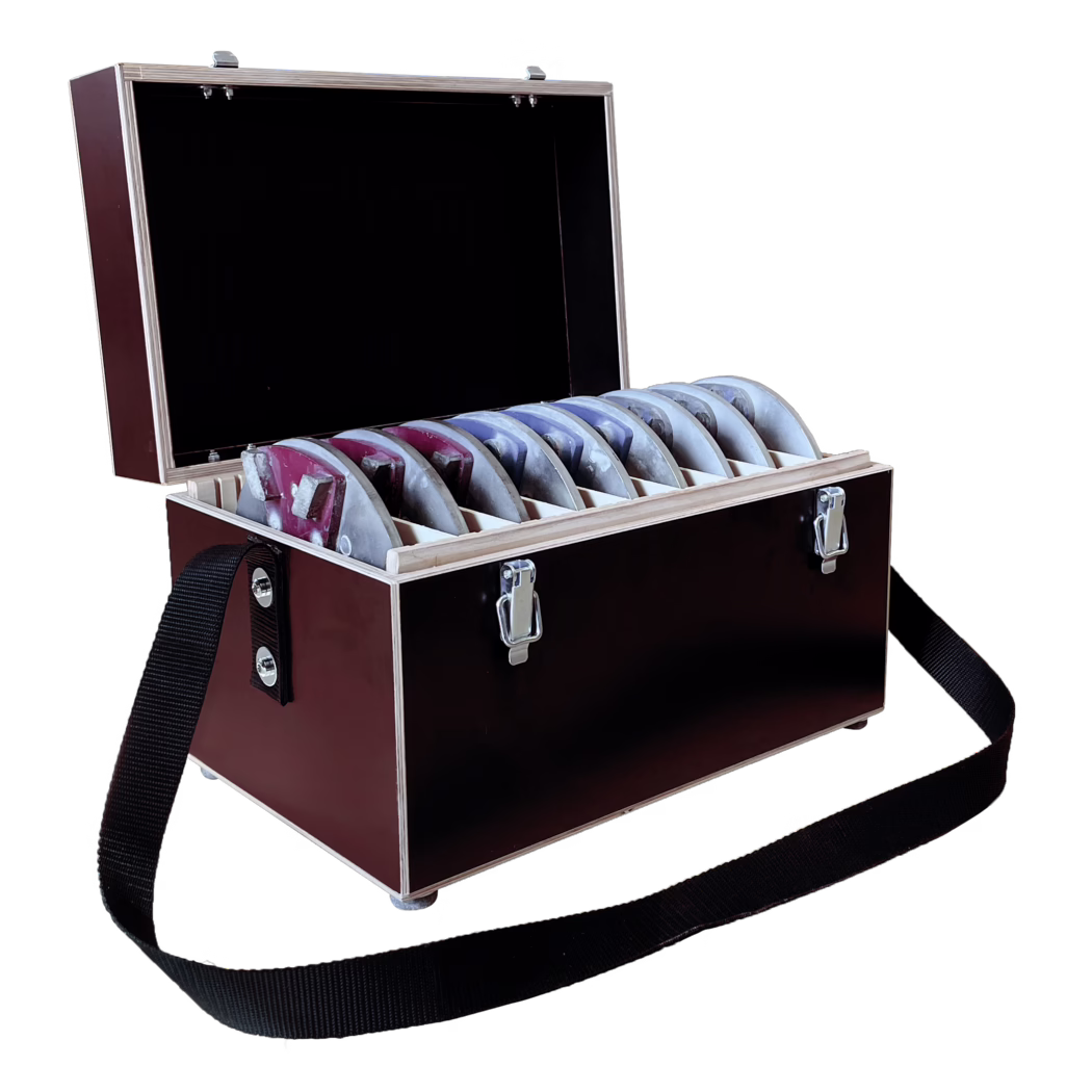 Derendinger_Dummy_10839_Zubehörbox_DSW-400-fräsen Offener dunkelbrauner Holzkoffer mit Metallverschlüssen und aufklappbarem Deckel, der ein schwarzes Innenleben zeigt; im Inneren eine Reihe gleichmäßig angeordneter halbkreisförmiger Metallplatten oder -formen mit roter und blauer Farbe, jeweils senkrecht in eigenen Holzeinsätzen gelagert; Gebrauchsspuren und abgeplatzte Farbreste sichtbar; schwarzer gewebter Tragegurt an der Seite befestigt; Nahaufnahme vor weißem Hintergrund.